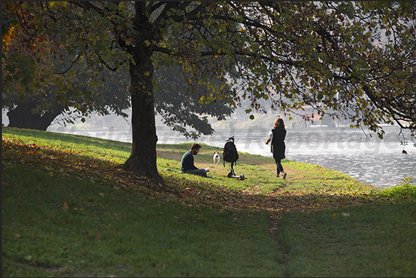 During the work lunch break, many people relax by observing the calm waters of Po river in front of the rowing clubs During the work lunch break, many people relax by observing the calm waters of Po river in front of the rowing clubs