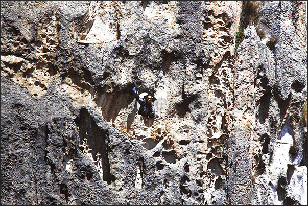 The guide leans out of the hole in the rock face waving his hat to be seen The guide leans out of the hole in the rock face waving his hat to be seen
