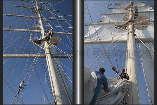 A sailor climbs the rope ladder that leads to the top of the fore mast while other sailors, reassemble the sail on the main mast A sailor climbs the rope ladder that leads to the top of the fore mast while other sailors, reassemble the sail on the main mast