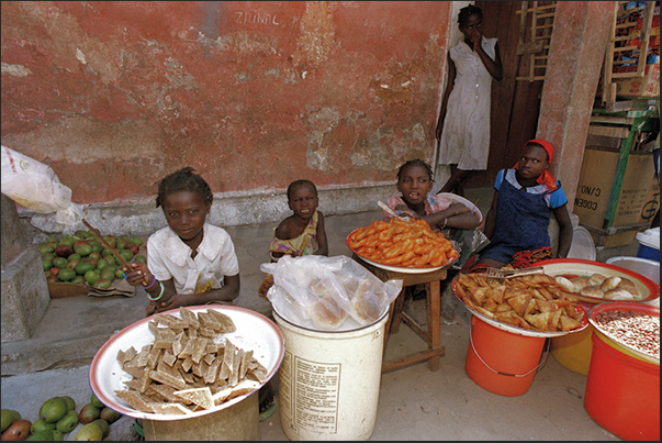 In the street, young women sell fruit, pastries and bread