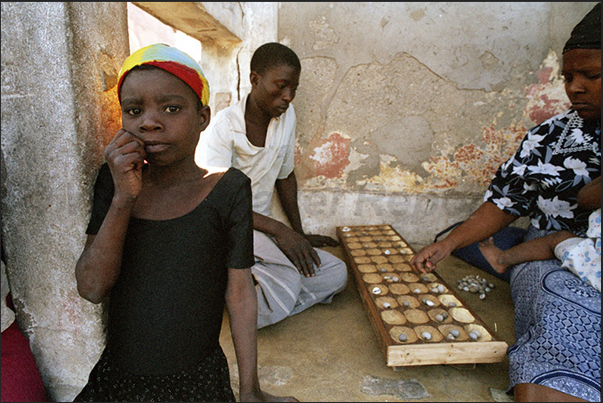 In front of the house, men play a ancient African game similar to backgammon
